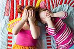 Portrait of two young sisters lying on blanket, covering face with hands