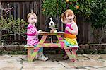 Two young sisters sitting on garden bench with pet dog