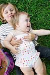Overhead view of female toddler lying on brother in garden