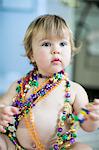 Female toddler trying on bead necklaces in kitchen