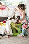 Female toddler removing laundry from child hiding in laundry basket