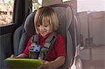 Girl in car safety seat looking at digital tablet