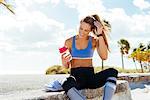 Young female runner sitting with takeaway drink on beach wall