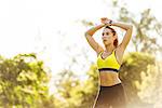 Exhausted young female runner with arms raised in park