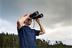 Senior man looking through binoculars toward coast of Maine, USA