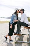 Pregnant mature couple kissing at park bench on coast