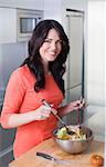 Pretty brunette woman preparing a salad in the kitchen smiling at camera