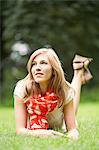 Portrait of a blonde woman lying down in the park, smiling and pensive