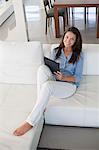 Pretty brunette woman on a couch with tablet smiling at camera