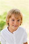 Portrait of a cute blond boy in park smiling at camera