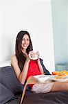 Pretty bruntette woman having breakfast in bed smiling at camera