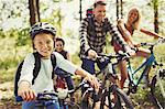 Portrait smiling girl mountain biking with family in woods