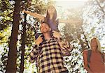 Father carrying daughter on shoulders, hiking in sunny woods