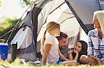 Smiling family talking and relaxing outside sunny tent