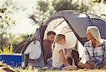 Family talking and relaxing outside tent at sunny campsite