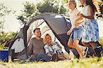 Parents watching happy daughters running around sunny campsite tent