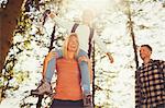 Mother carrying daughter on shoulders hiking in sunny woods