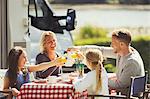 Family toasting coffee and orange juice glasses at table outside sunny motor home