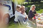 Happy, affectionate father and daughter hugging outside sunny motor home