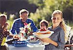 Portrait smiling girl serving strawberry cake to family at sunny garden party patio table