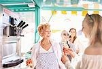 Smiling senior female business owner serving ice cream to young woman at food cart