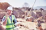 Construction worker foreman talking on walkie-talkie at sunny construction site