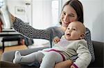 Smiling mother holding baby daughter and taking selfie with camera phone