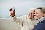 Senior couple taking selfie with cell phone on windy winter beach