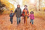 Portrait smiling young family holding hands walking on path in autumn park