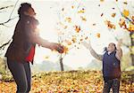 Playful mother and daughter throwing autumn leaves in sunny park