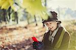 Smiling senior woman using cell phone in sunny autumn park