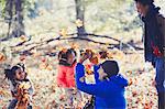 Playful father and daughters throwing autumn leaves in sunny woods