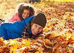 Portrait playful daughter laying on father in autumn leaves in sunny park