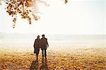 Silhouette senior couple holding hands walking in sunny autumn park