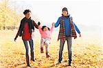 Parents swinging daughter in sunny autumn park grass