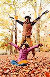 Playful mother and daughter throwing autumn leaves in park