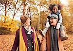 Laughing senior couple carrying daughter on shoulders in autumn woods