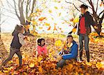 Young family playing in autumn leaves in sunny park