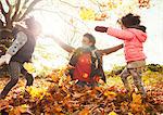 Playful mother and daughters throwing autumn leaves in sunny park