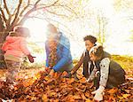 Young family playing in autumn leaves in sunny park