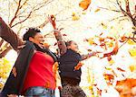 Playful mother and daughter throwing autumn leaves in sunny park