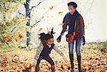 Playful mother and daughter throwing autumn leaves in sunny park