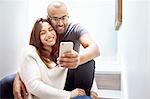Smiling couple with camera phone taking selfie on stairs