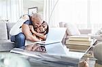 Playful couple hugging and using laptop in living room