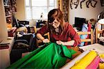 A woman ripping brightly coloured material on a tabletop in a workroom.