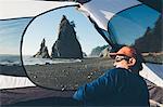 Man sitting in camping tent, Rialto Beach in distance, Olympic National Park, Washington, USA.