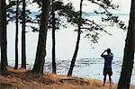 Man standing on a beach, looking through binoculars, San Juan Islands in the distance, Washington, USA.