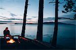 Man sitting by campfire at dusk, San Juan Islands in the distance, Washington, USA.