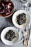 Overhead view of squid ink spaghetti dish and radicchio lettuce in bowl