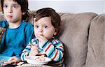 Baby boy and big brother sitting on sofa watching TV while eating a snack